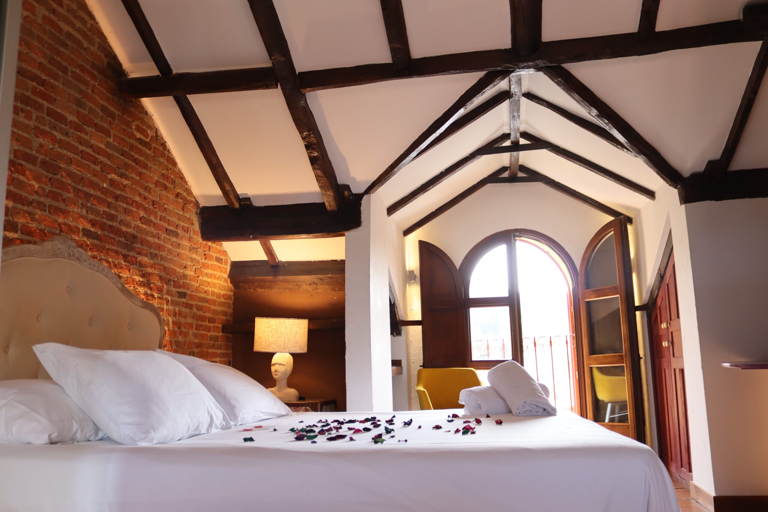 Cama, techo abuhardillado y balcón de Suite El Torreón
